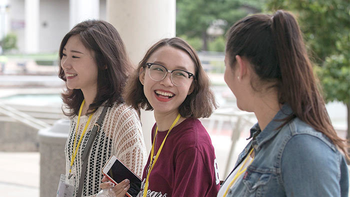 Three students smiling, talking and walking together on campus